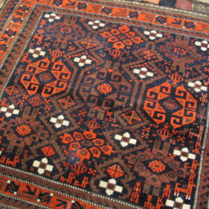 Intricate geometric rug in deep navy and fiery orange, framed by complex borders on wood plank flooring.