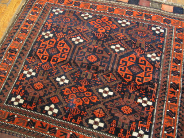 Intricate geometric rug in deep navy and fiery orange, framed by complex borders on wood plank flooring.