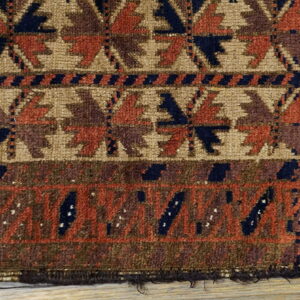 Detail of a medium-pile geometric rug in tan, rust, and navy blue resting on wood planks.
