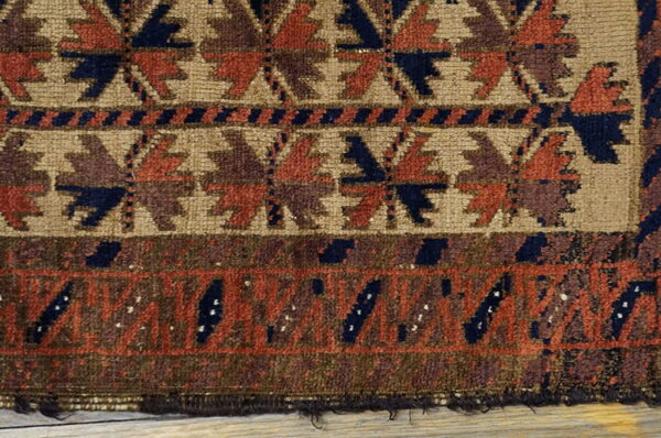 Detail of a medium-pile geometric rug in tan, rust, and navy blue resting on wood planks.