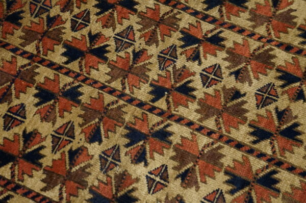 Geometric star and diagonal line patterns in rust, navy, and brown cover the low pile tan rug.