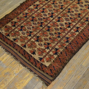 Geometric tan rug with repeating rust and navy patterns rests diagonally on distressed wooden flooring.
