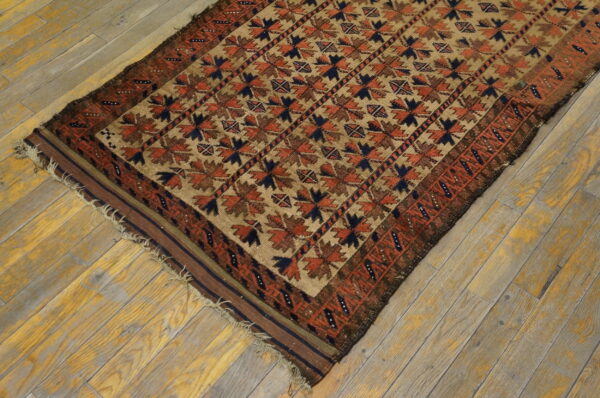 Geometric tan rug with repeating rust and navy patterns rests diagonally on distressed wooden flooring.