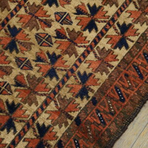 Close-up shows a tan rug with terracotta, navy, and brown geometric patterns lying on light wood.