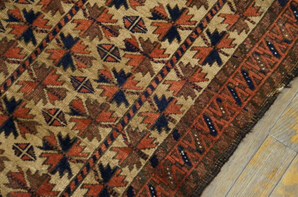 Close-up shows a tan rug with terracotta, navy, and brown geometric patterns lying on light wood.