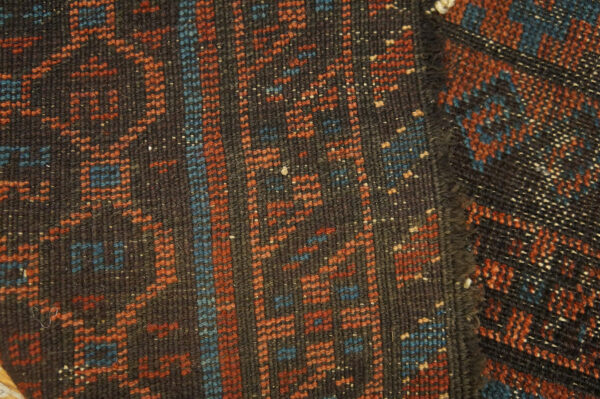 Dense, dark brown rug surface with contrasting geometric patterns in rust orange and blue.