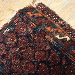 Red and dark blue textured rug corner with cream fringe visible on rustic wooden floorboards.