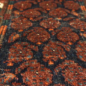 High-pile rug closeup showing deep red geometric guls on a dark navy ground with orange and teal detail.