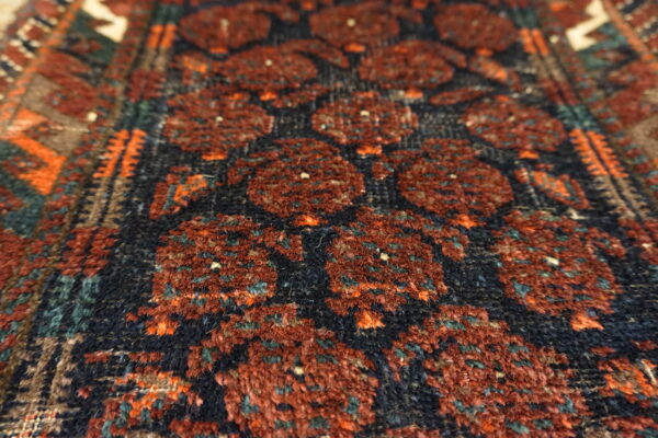 High-pile rug closeup showing deep red geometric guls on a dark navy ground with orange and teal detail.