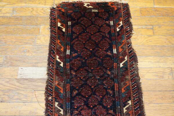 Narrow runner rug with deep red medallions on a navy field, bordered by orange and teal, resting on wood floorboards.