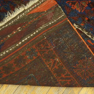 A dark red and navy patterned rug is folded on a wood floor, exposing the woven backing.