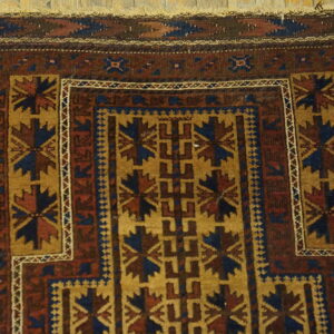 Close-up of a maroon, blue, and gold patterned rug lying on light wood floorboards.
