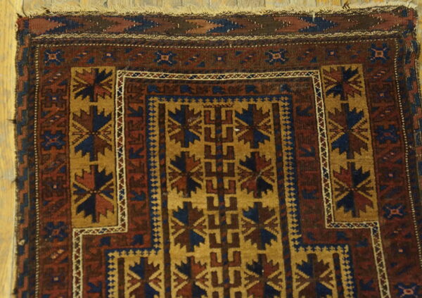 Close-up of a maroon, blue, and gold patterned rug lying on light wood floorboards.