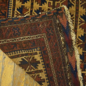 Close-up of a geometric red, blue, and tan rug folded over on distressed hardwood flooring.