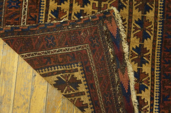 Close-up of a geometric red, blue, and tan rug folded over on distressed hardwood flooring.
