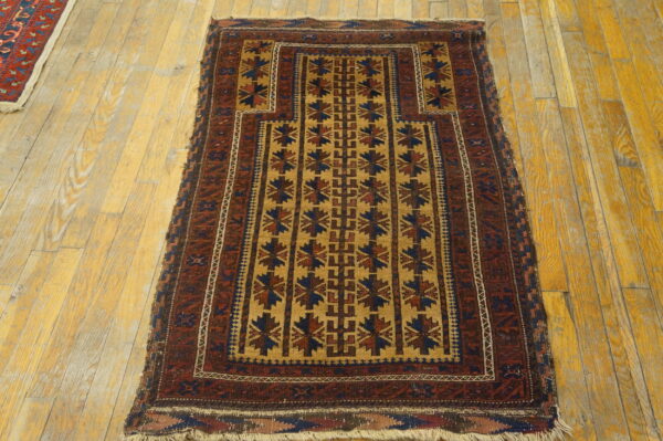 Red and gold geometric pattern rug with low pile lying on distressed yellow wood floorboards.