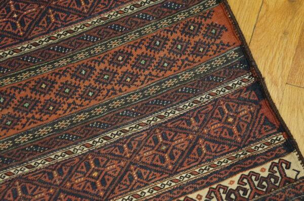 Terracotta and navy rug with repeating geometric banded patterns rests on light hardwood flooring.