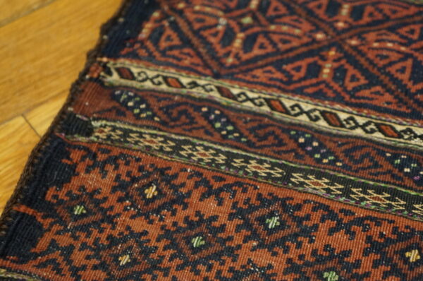 Geometric rug in dark red and navy blue rests on light wood planks, showing complex borders.