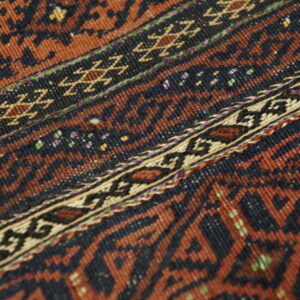 Low-pile rug detail showing bands of rust and dark brown geometric patterns with colorful accents.