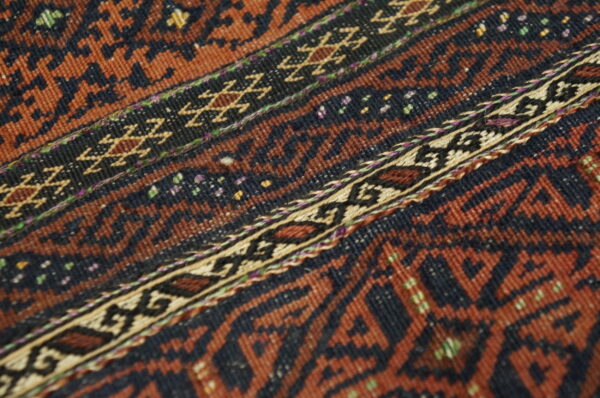 Low-pile rug detail showing bands of rust and dark brown geometric patterns with colorful accents.