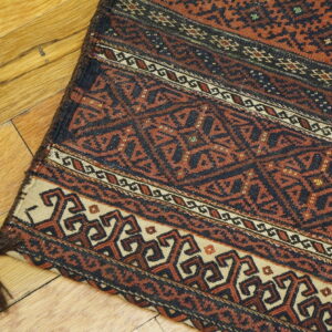 Geometric flatweave rug featuring rust, black, and cream tribal patterns resting diagonally on a polished wood floor.