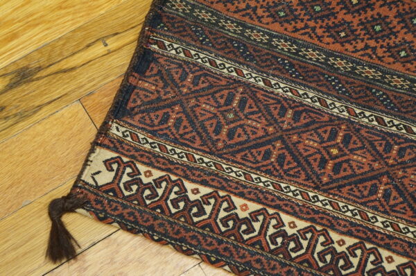 Geometric flatweave rug featuring rust, black, and cream tribal patterns resting diagonally on a polished wood floor.