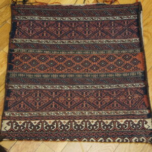 Geometric, flat-woven rug in deep rust and navy on a light wood plank floor.