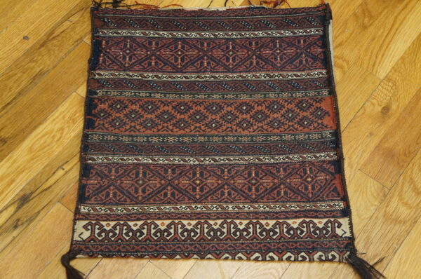 Geometric, flat-woven rug in deep rust and navy on a light wood plank floor.