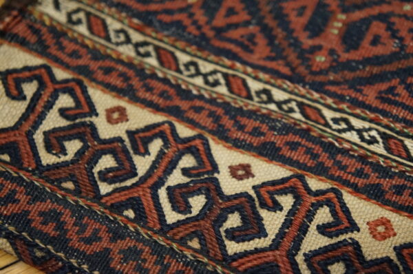 Close-up shows a flatwoven rug with geometric bands in navy, rust, and light tan colors.