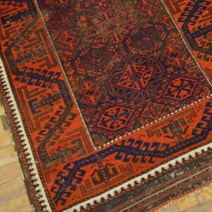 Red and navy geometric rug with dense tribal motifs resting on distressed light wooden flooring.