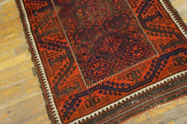 Red and navy geometric rug with dense tribal motifs resting on distressed light wooden flooring.