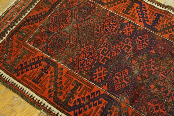 A close-up of a rustic red and navy geometric patterned rug lying on light hardwood flooring.