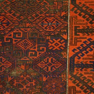 Red and navy geometric patterned rug detailed with tribal motifs resting on light wood plank flooring.