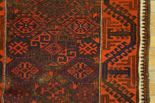 Red and navy geometric patterned rug detailed with tribal motifs resting on light wood plank flooring.