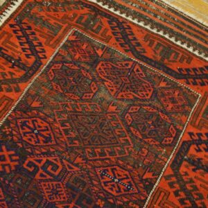 Geometric red and indigo rug with detailed central motifs lying diagonally on light wood flooring.
