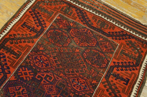 Geometric red and indigo rug with detailed central motifs lying diagonally on light wood flooring.
