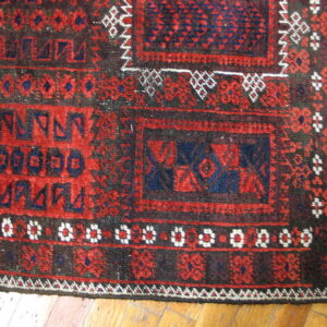 Geometric rug in red, dark blue, and black laid across light brown hardwood planks.