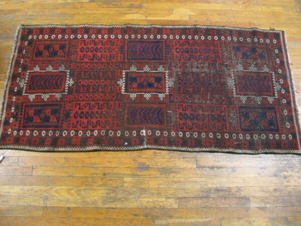 Low-pile red and dark blue distressed runner rug featuring geometric panels on plank wood floors.