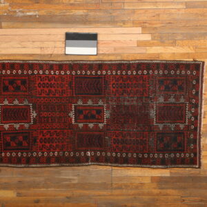 Geometric runner rug in deep red, black, and white colors is displayed on worn hardwood flooring.