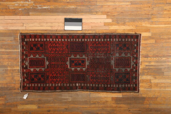 Geometric runner rug in deep red, black, and white colors is displayed on worn hardwood flooring.