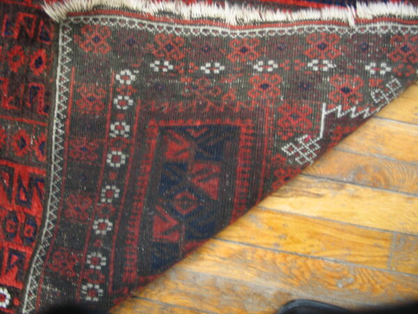 A dark red and brown geometric rug with white fringe laid diagonally on shiny hardwood floors.