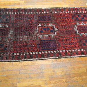 A distressed red and dark blue geometric runner rug lies on worn wooden plank floors.
