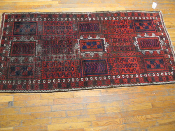 A distressed red and dark blue geometric runner rug lies on worn wooden plank floors.