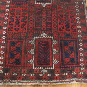 Rustic red and navy geometric rug with white accents rests on light wooden plank flooring.