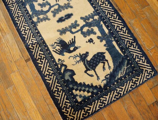 Blue and cream runner rug with a deer and bird pictorial pattern sits on light brown plank flooring.