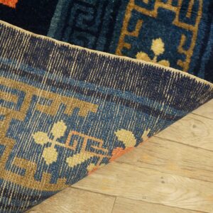 A dark blue and tan patterned rug is folded back, showing the woven reverse on light wood floors.