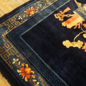 High-pile navy rug corner with coral and gold floral patterns rests on distressed light wood planks.