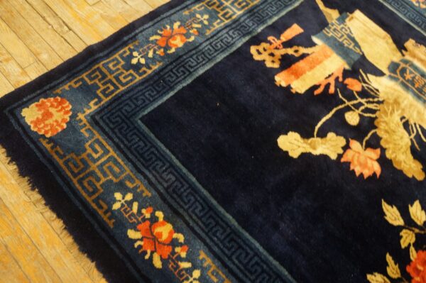 High-pile navy rug corner with coral and gold floral patterns rests on distressed light wood planks.