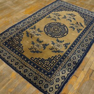 Tan and navy rug with geometric borders and floral motifs on aged, distressed wood flooring.