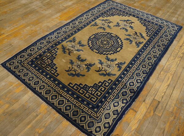 Tan and navy rug with geometric borders and floral motifs on aged, distressed wood flooring.